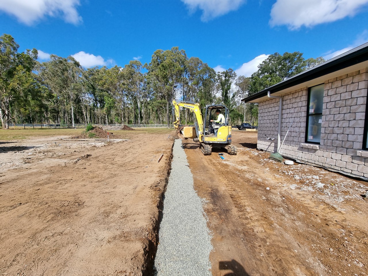 Excavator laying drainage trench beside new build