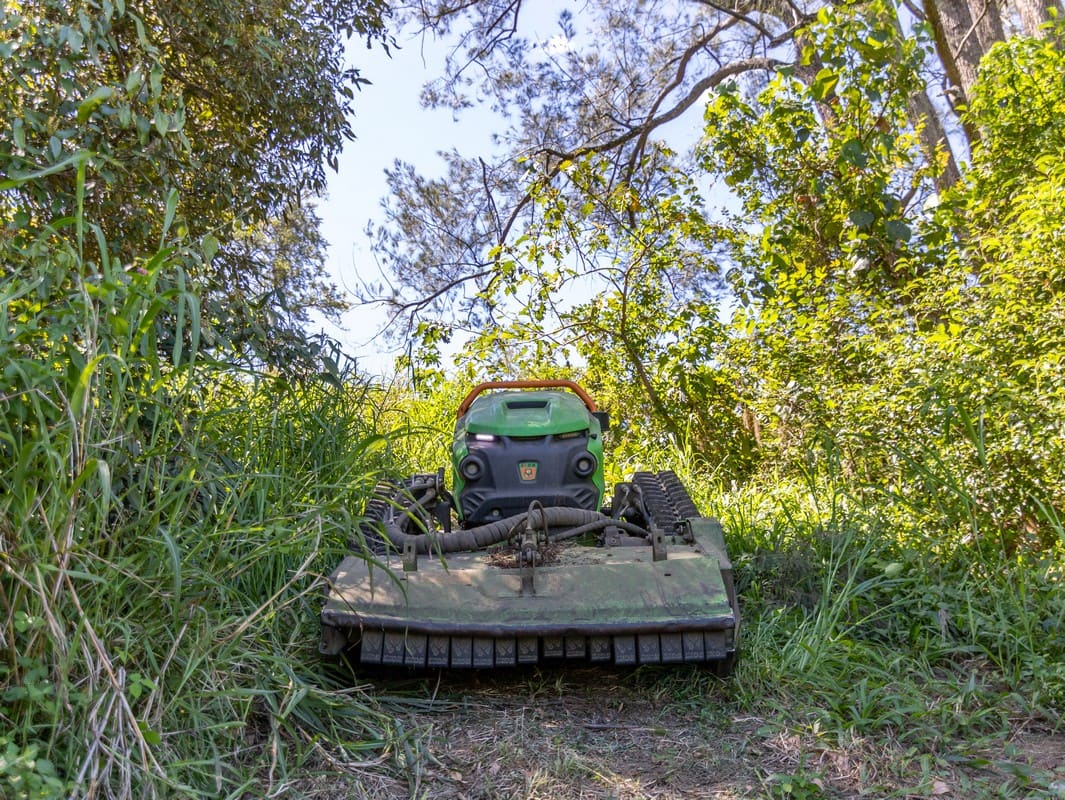 Remote slope mower clearing dense scrub on steep terrain