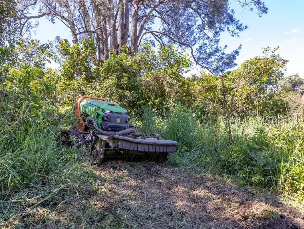 Remote slope mower clearing dense vegetation on steep terrain