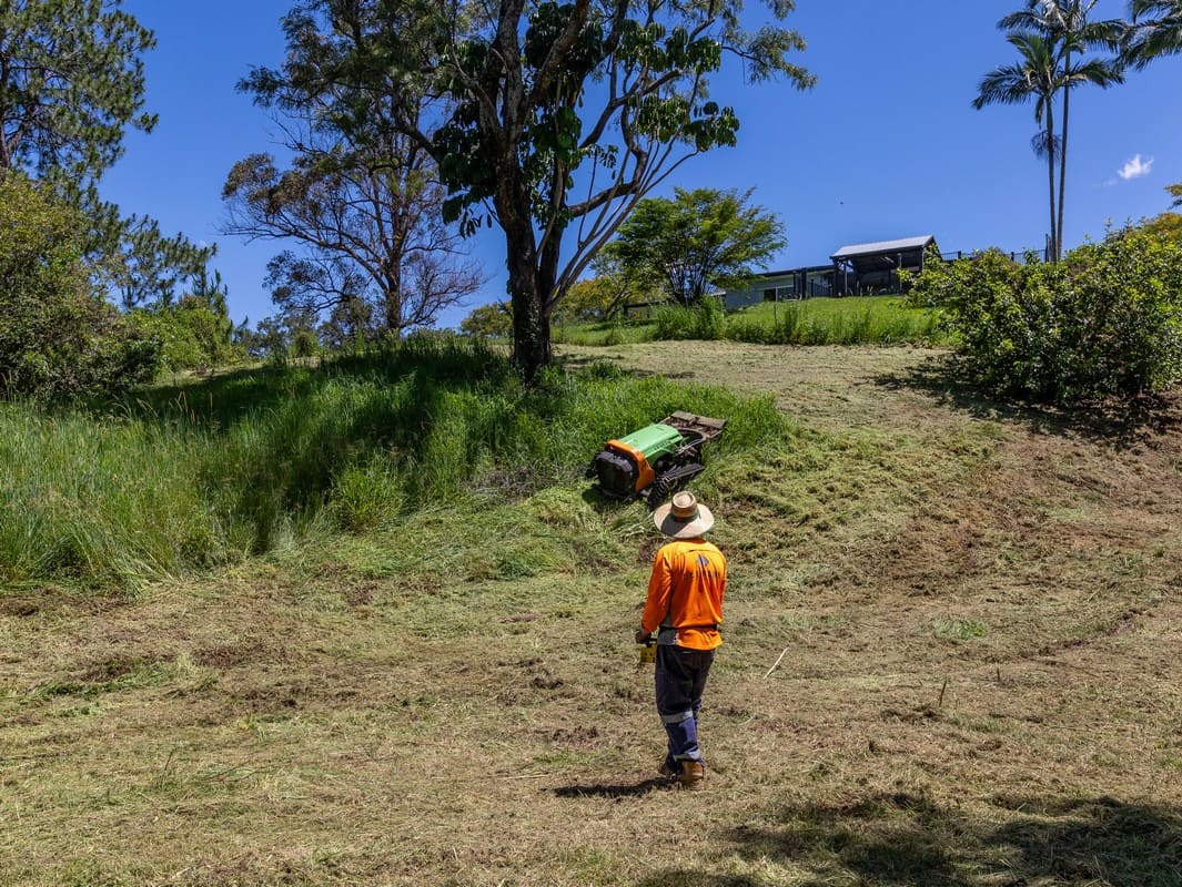 Operator controlling remote slope mower on hillside